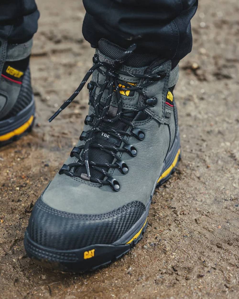 Dark Shadow Coloured Caterpillar Munising Safety Boot On A Muddy Background