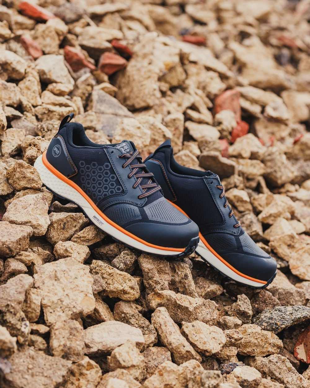 Black/Orange coloured Timberland Pro Reaxion Composite Safety Trainers on stone background