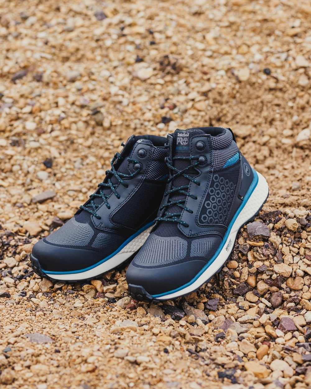 Black/Blue coloured Timberland Pro Reaxion Mid Composite Safety Boots on rocky background