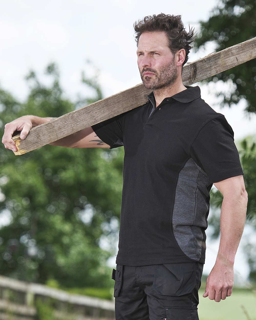 Black Coloured TuffStuff Pro Work Polo Shirt On A Garden Background