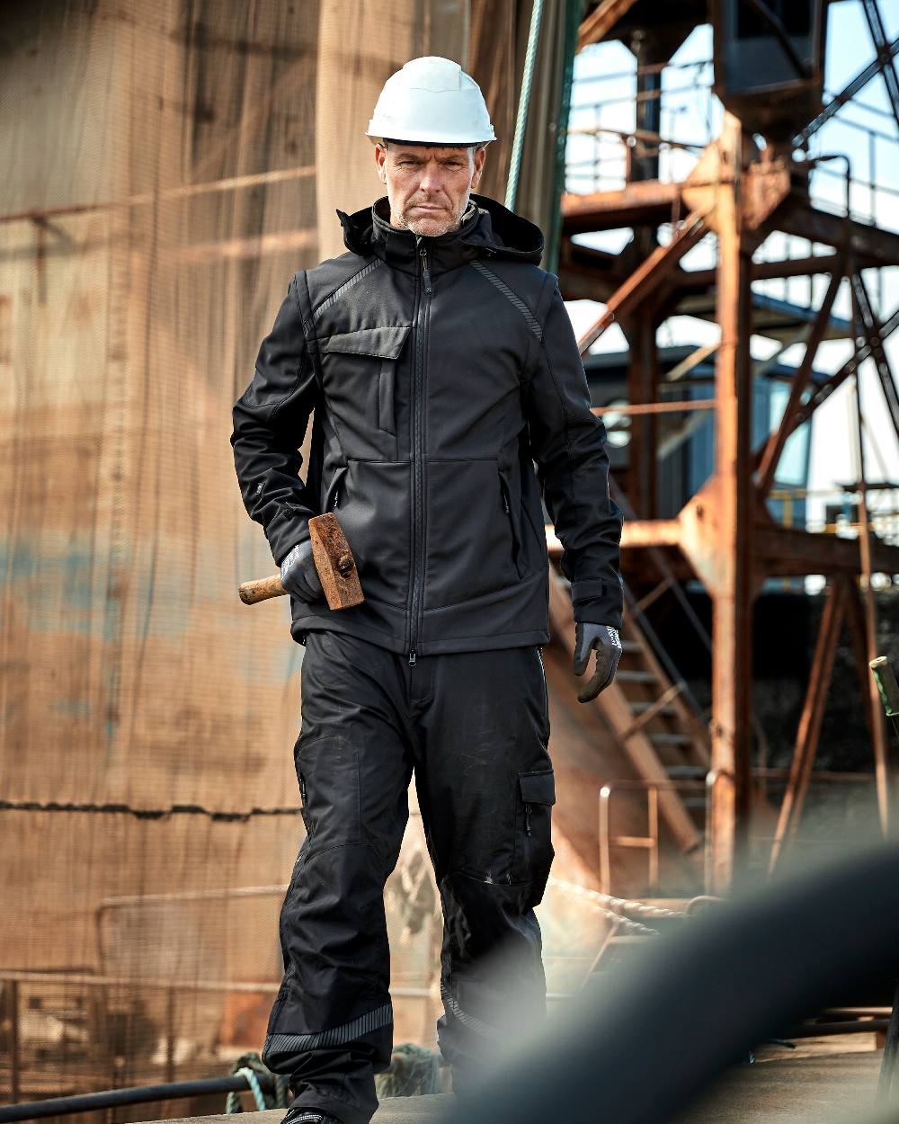 Black Coloured Elka Mens Working Xtreme Softshell Jacket With Detachable Sleeves on construction background 