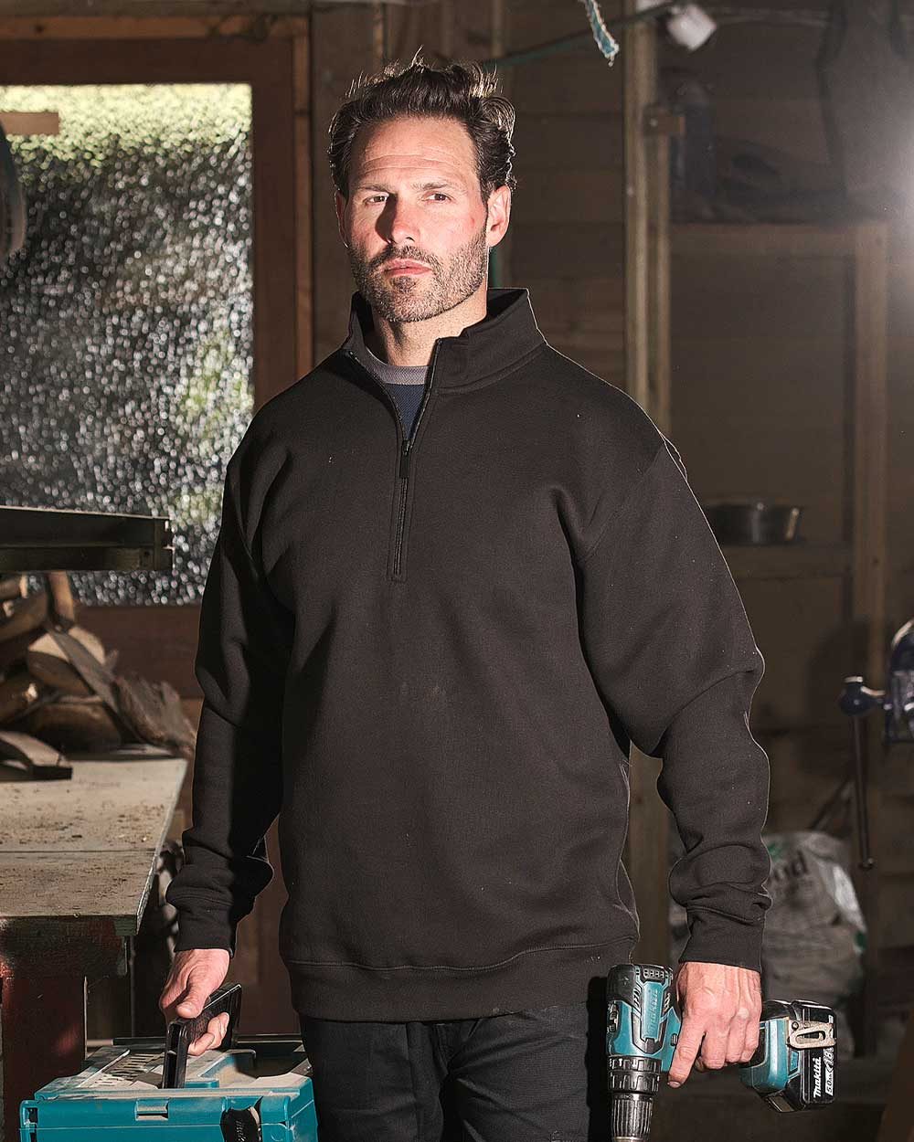 Black coloured Fort Workforce 1/4 Zip Sweatshirt on workshop background 