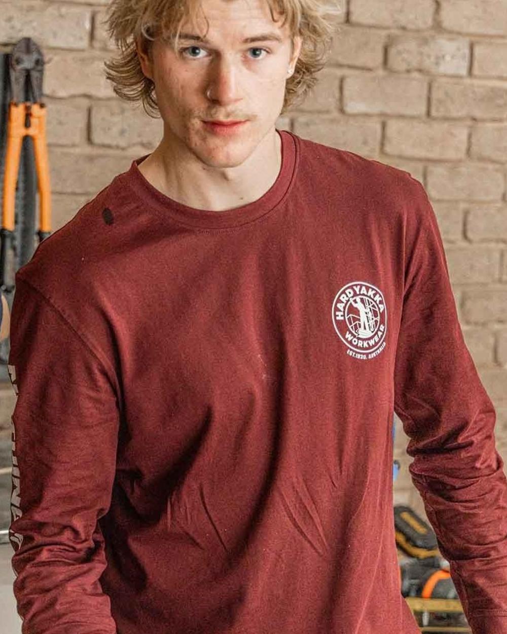 Burgundy coloured Hard Yakka Heritage Long Sleeve T-Shirt on house background 