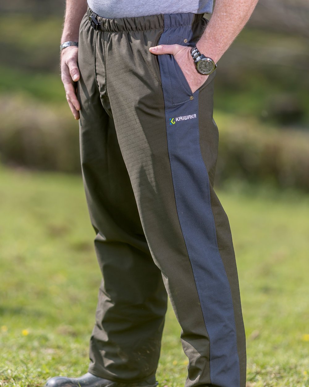 Olive coloured Kaiwaka Mens Stormforce Overtrousers on grassy background 