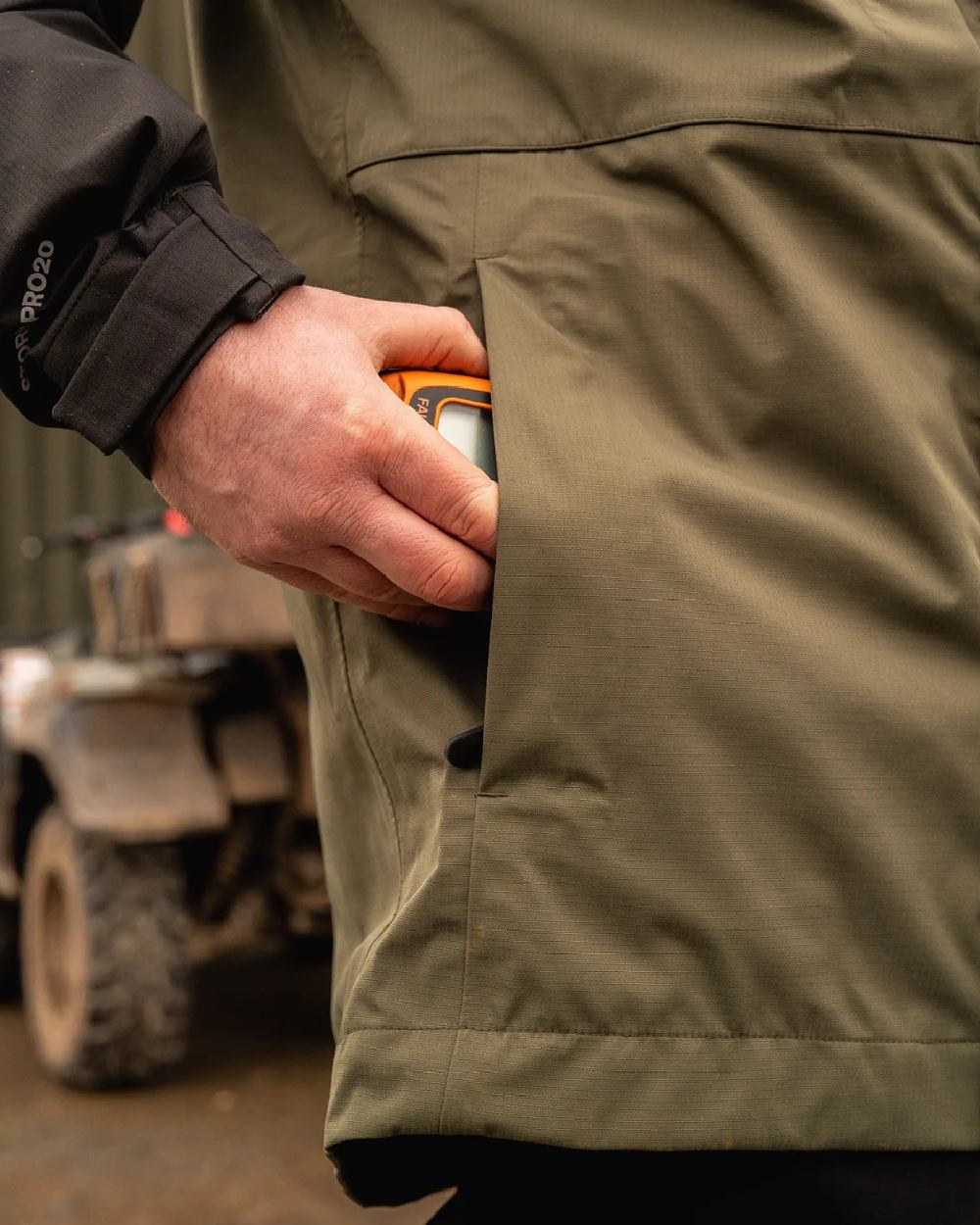 Moss Black Coloured Line 7 Mens Territory Storm Pro20 Waterproof Jacket on blurry background 