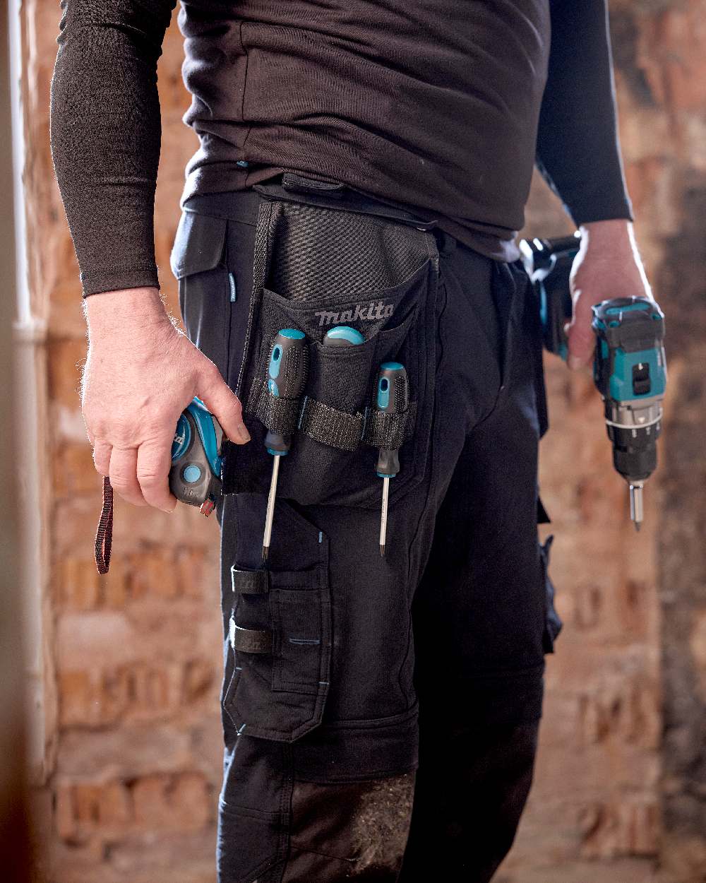 Black Coloured Makita Mens Onyx Stretch Trousers on construction background 