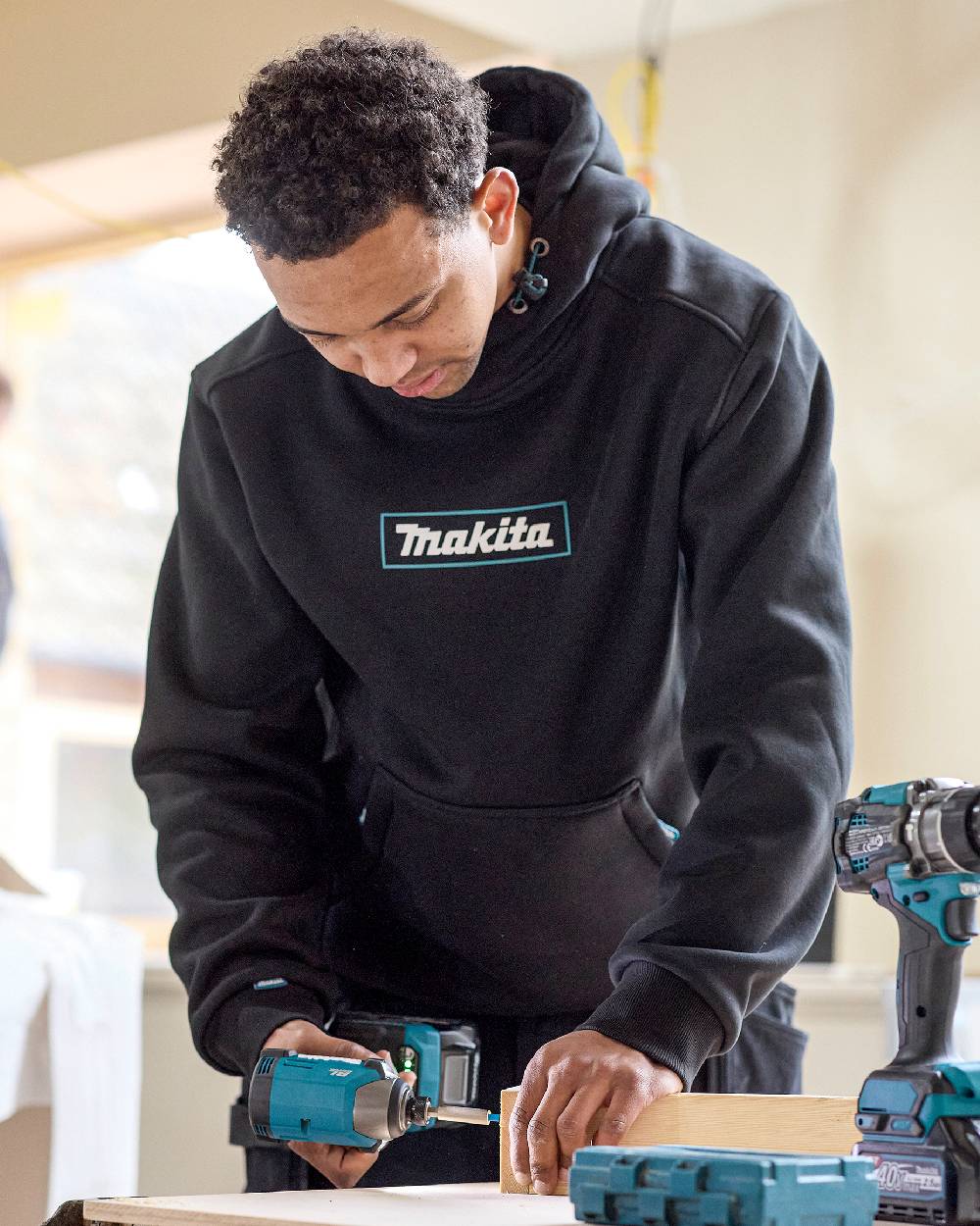 Black Coloured Makita Mens Origin Hoodie on construction background 