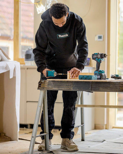 Black Coloured Makita Mens Origin Hoodie on construction background 