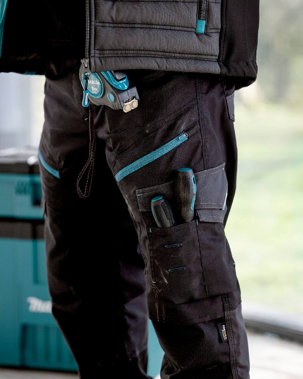 Black Coloured Makita Mens Vector Stretch Trousers on outdoor background 