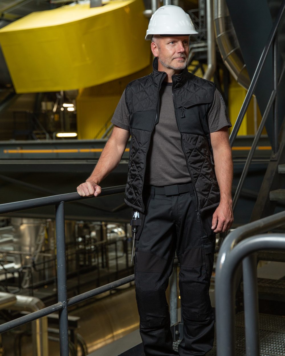 Black Coloured Mascot Workwear Mens Accelerate Lightweight Thermal Gilet on construction background 