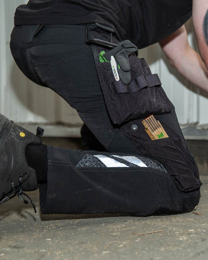 Black Coloured Mascot Workwear Mens Accelerate Lightweight Trousers With Holster Pockets on factory background 