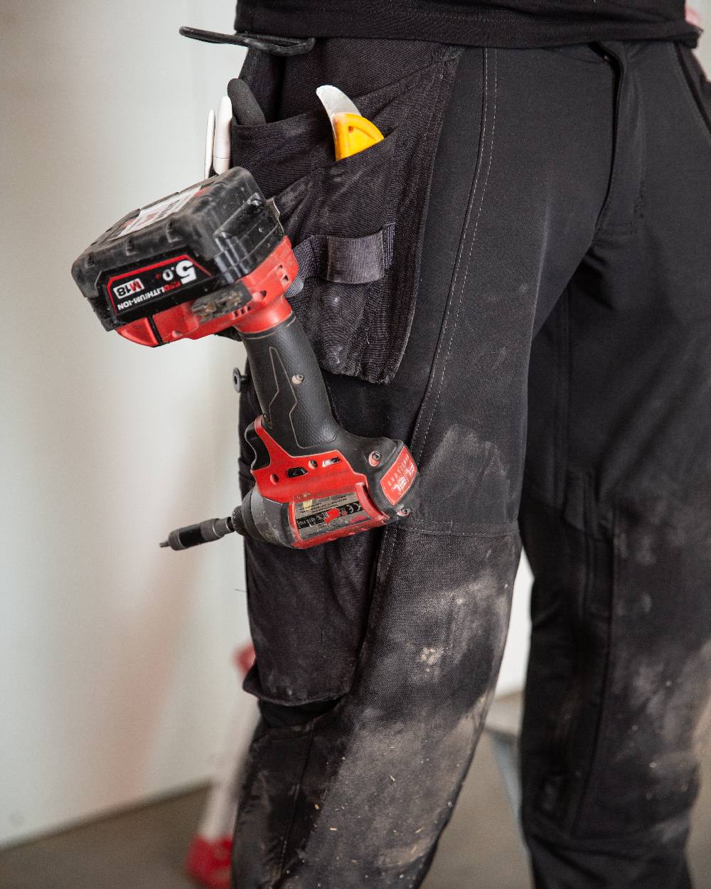 Black Coloured Mascot Workwear Mens Accelerate Lightweight Trousers With Holster Pockets on factory background 