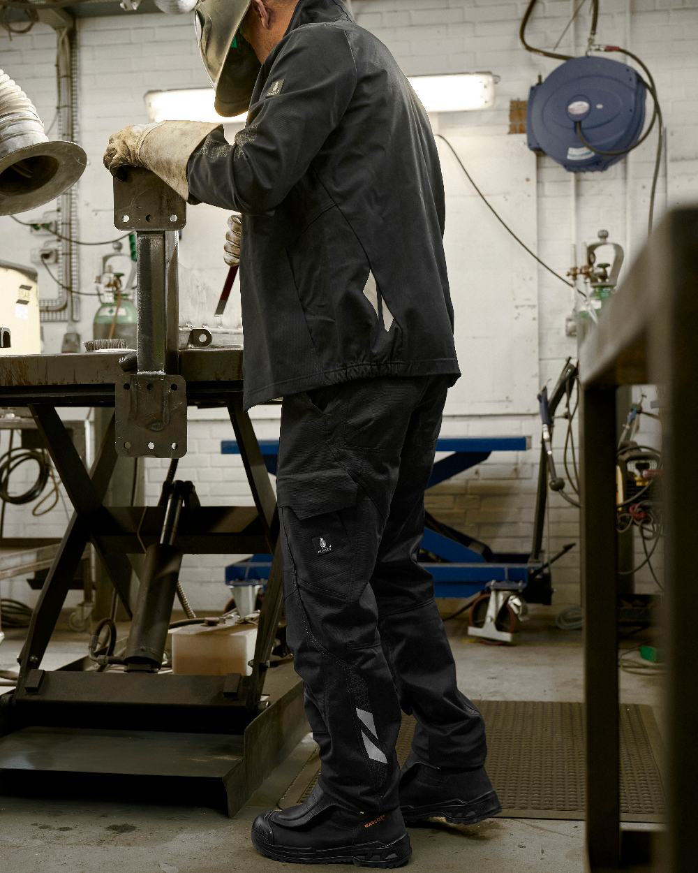 Black Coloured Mascot Workwear Mens Accelerate Organic Cotton Trousers on factory background 