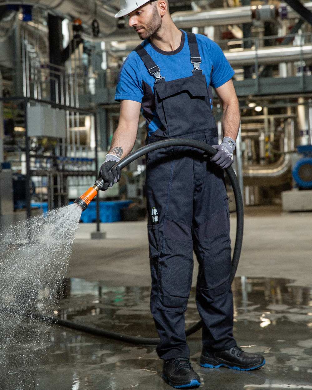 Dark Navy Coloured Mascot Workwear Mens Accelerate Stretch Zones Bib &amp; Brace With Kneepad Pockets on factory background 