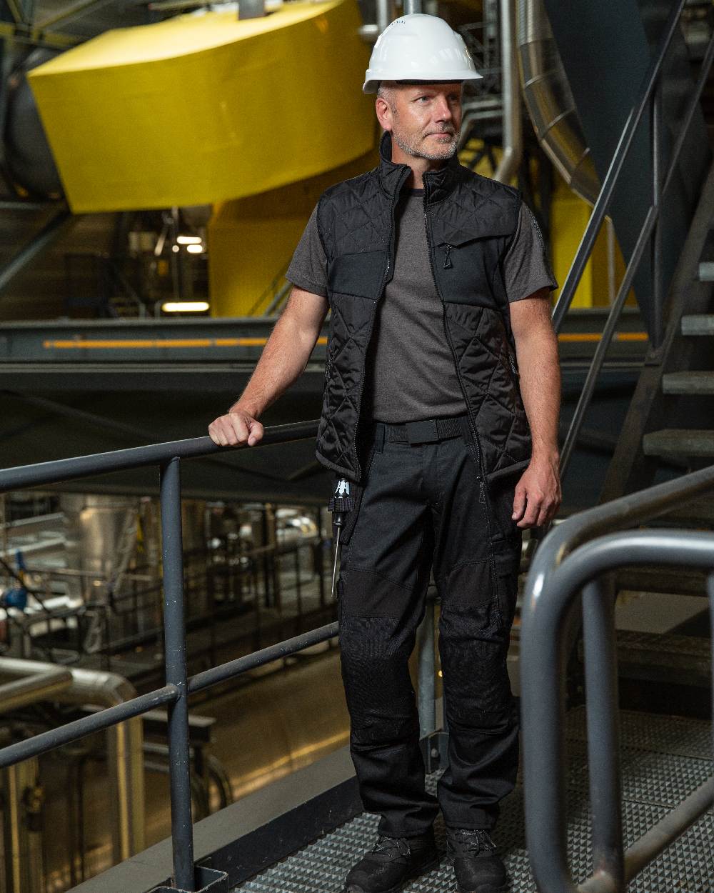 Black Coloured Mascot Workwear Mens Accelerate Trousers With Holster Pockets on factory background 