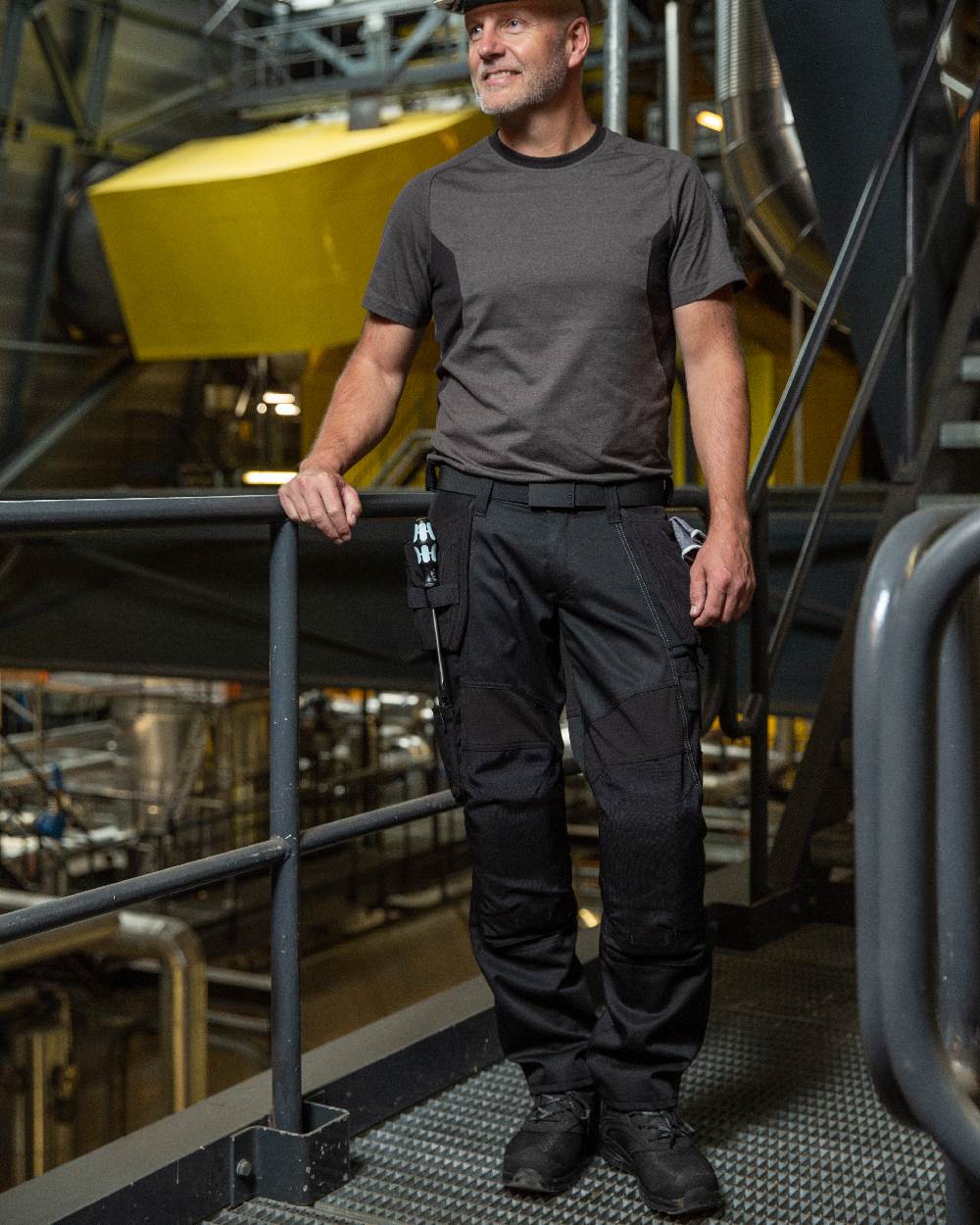 Black Coloured Mascot Workwear Mens Accelerate Trousers With Holster Pockets on factory background 
