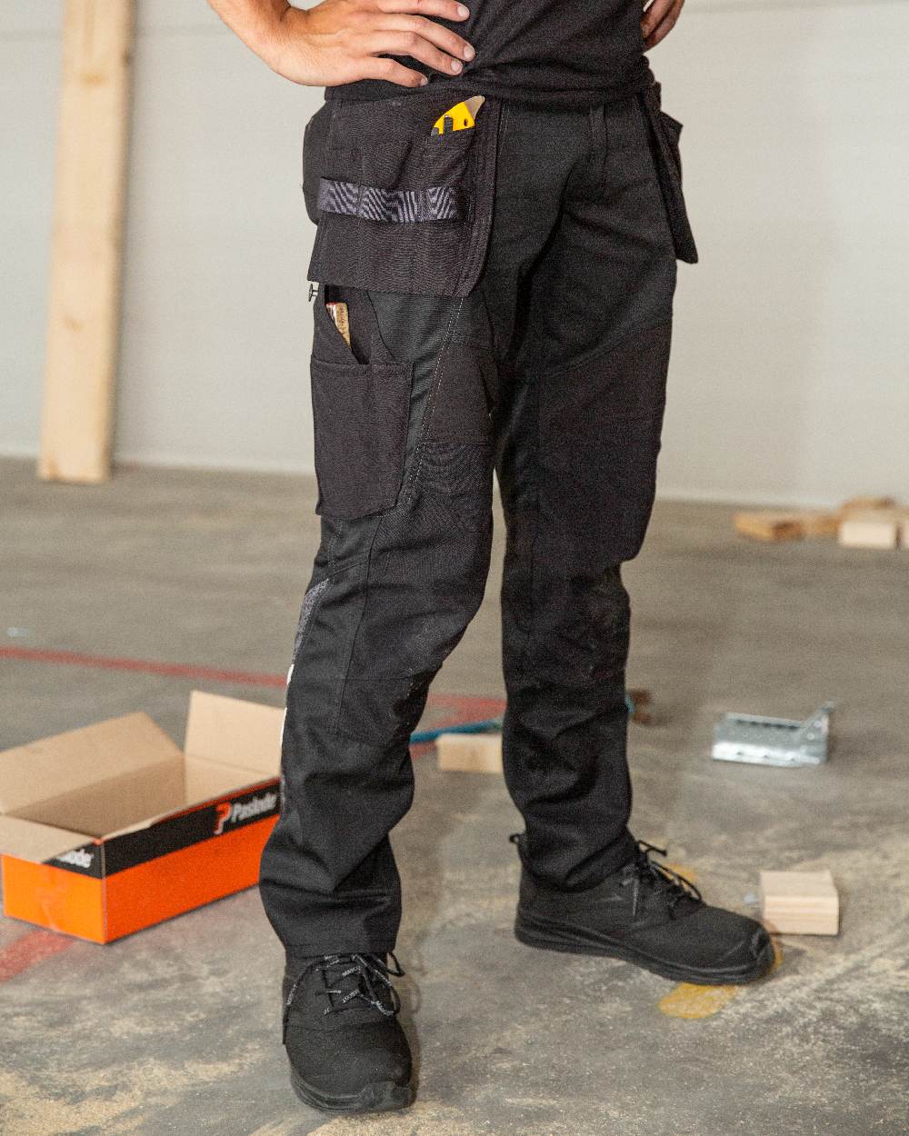 Black Coloured Mascot Workwear Mens Accelerate Trousers With Holster Pockets on factory background 