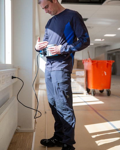 Dark Navy Coloured Mascot Workwear Mens Accelerate Ultimate Stretch Trousers With Kneepad Pockets on construction background 