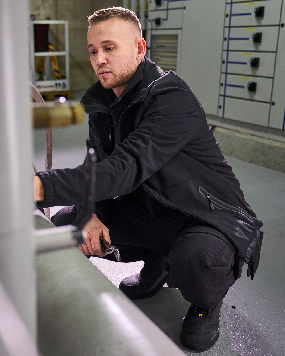 Black Coloured Mascot Workwear Mens Customized Breathable Softshell Jacket on factory background 