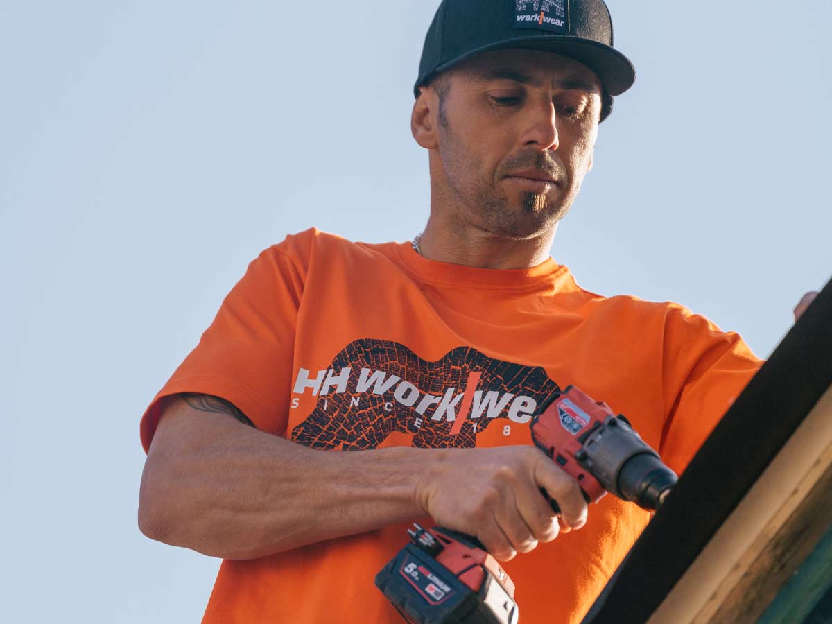 Work T-shirts. Man in orange t-shirt drilling a hole.