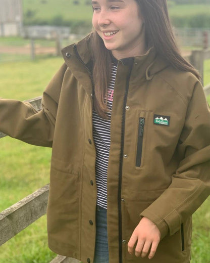 Teak coloured Ridgeline Kids Monsoon Classic Jacket on farm background 