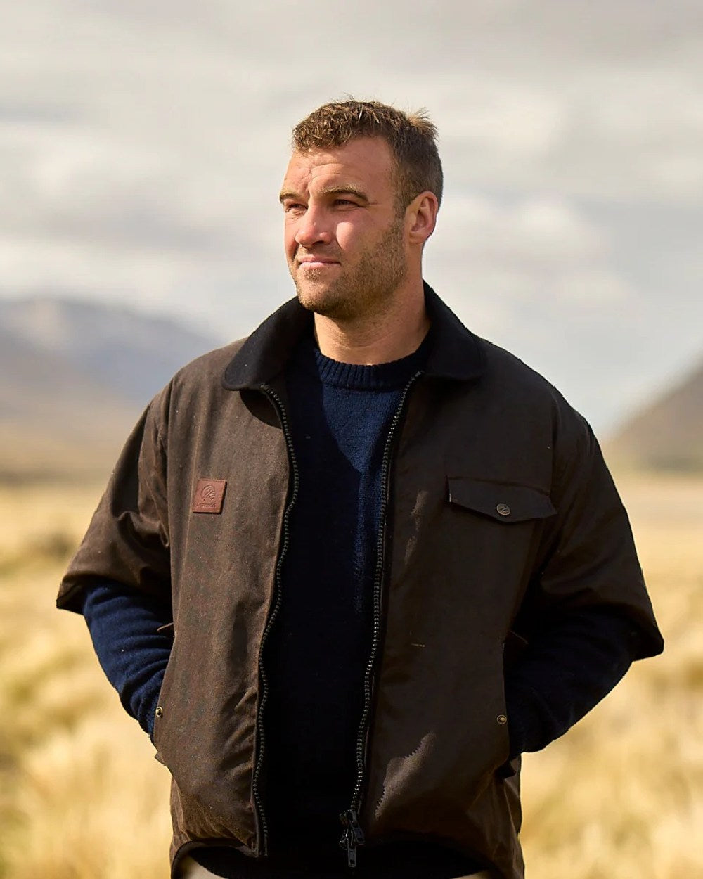 Brown Coloured Swanndri Mens 3/4 Sleeve Oilskin Jacket on field background 