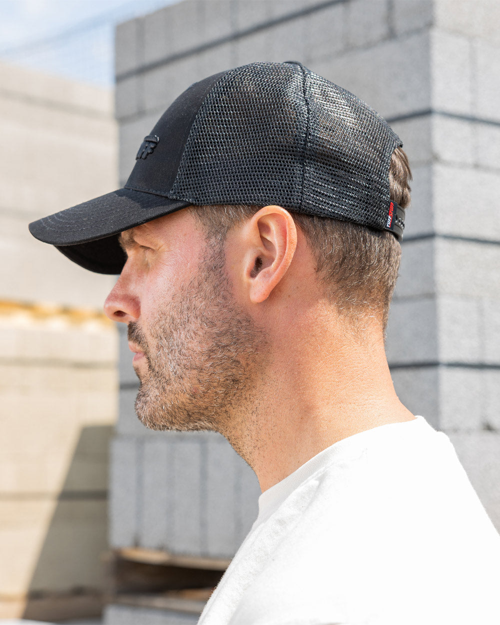 Black coloured TuffStuff Trucker Cap on Model with construction background 