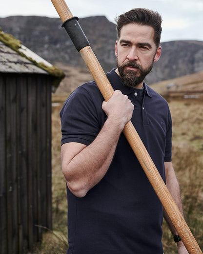 Navy coloured Hoggs of Fife Largs Pique Polo Shirt on barn background 