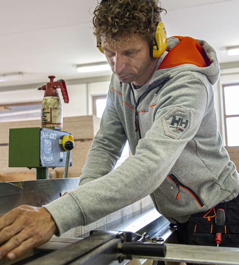 Man with ear defenders cuts wood wearing a grey Helly Hansen hoodie