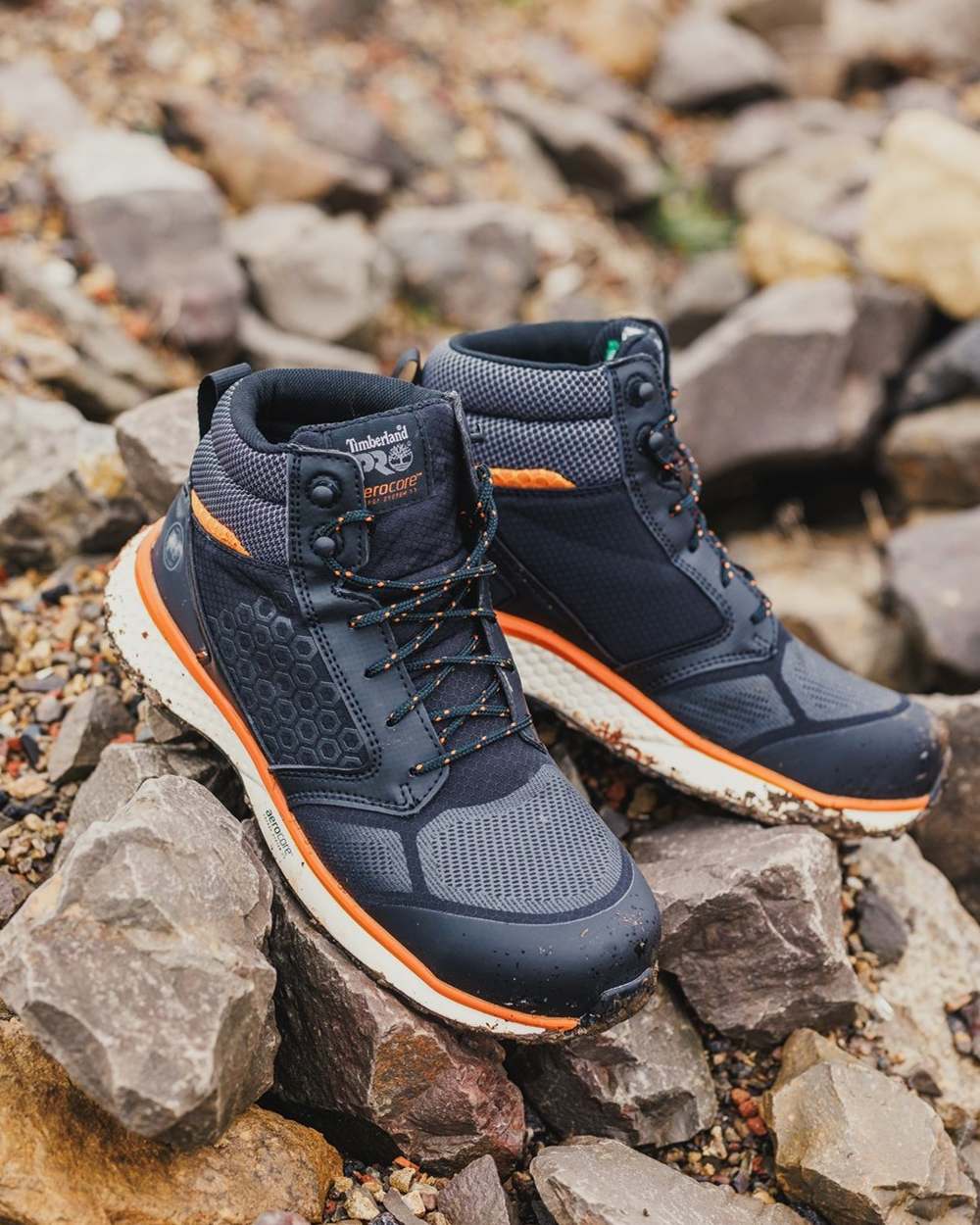 Black/Orange coloured Timberland Pro Reaxion Mid Composite Safety Boots on rocky background