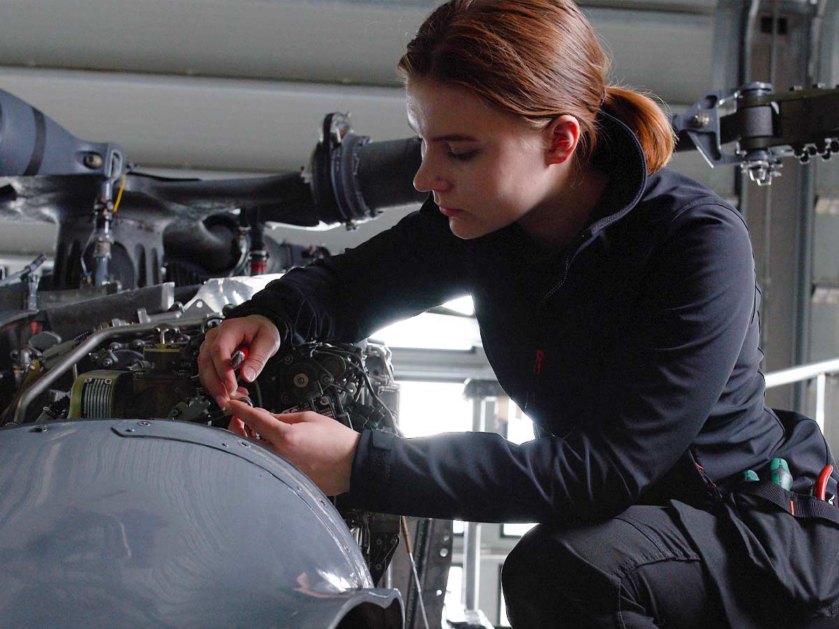 WOMEN'S WORKWEAR. Woman in fleece top working on a helicopter engine.