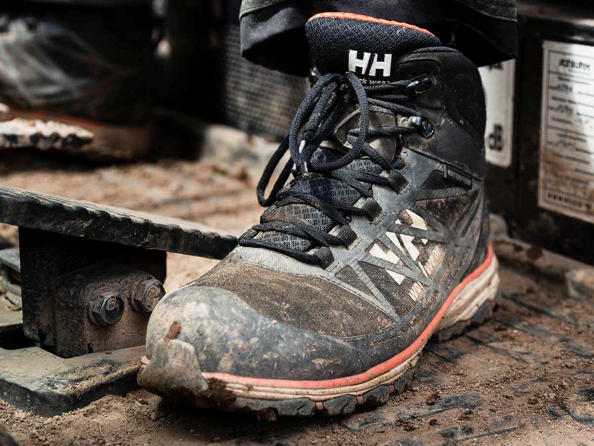 Work Boots. Helly Hansen lace up safety boots in black with orange trim on muddy floor.